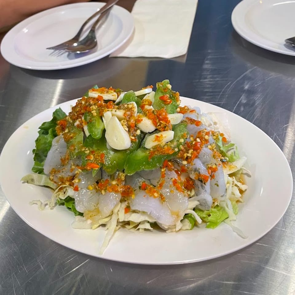 Thai shrimp salad with garlic, chili, and bitter melon on a white plate.