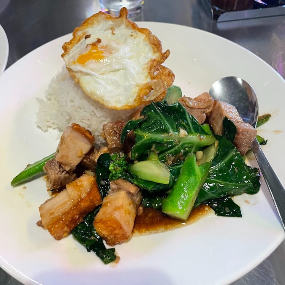 Thai crispy pork belly with kale and a fried egg over rice on a white plate.