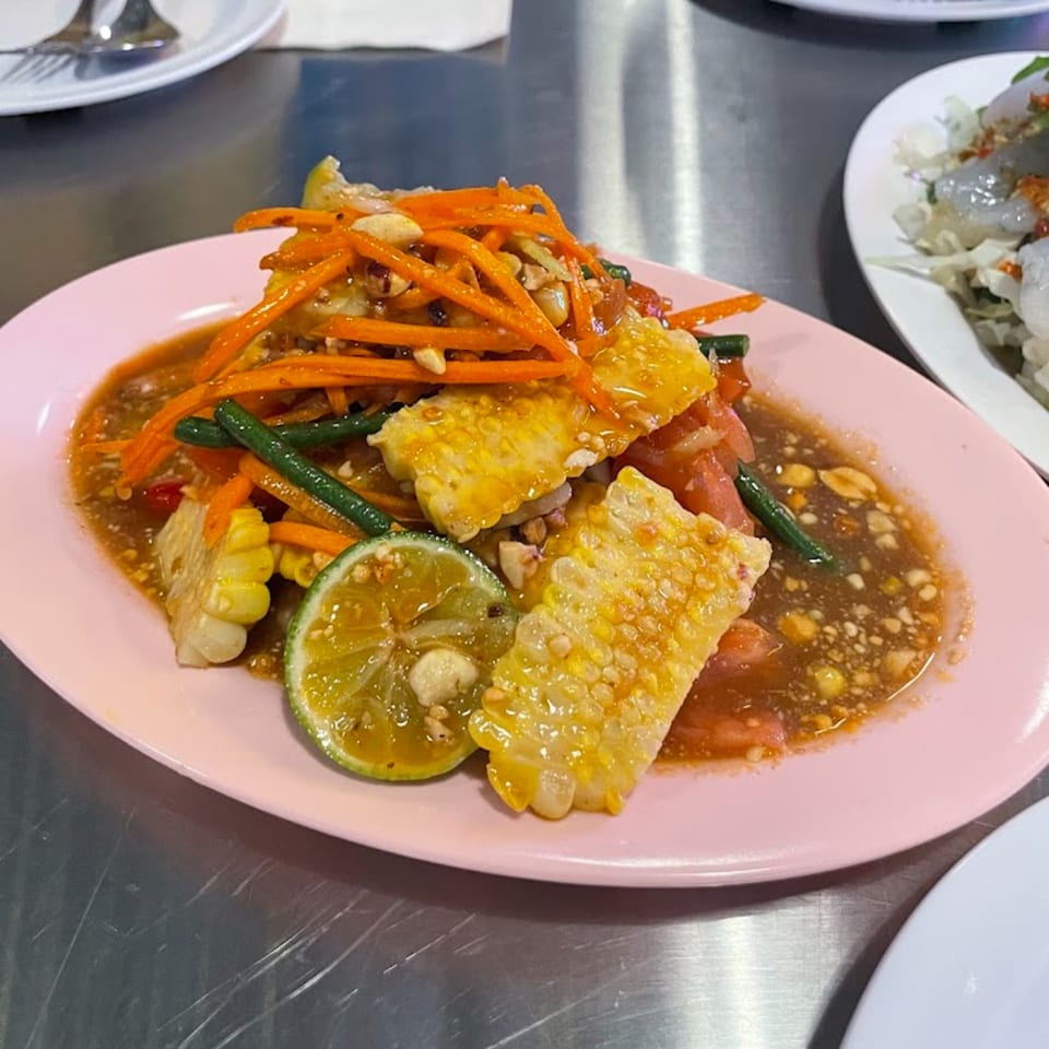 A vibrant Thai salad with shredded carrots, corn, green beans, and lime on a pink plate.