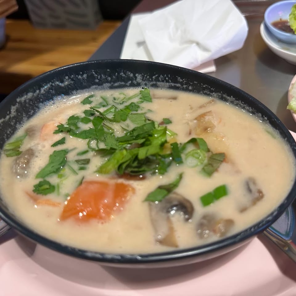 Creamy Tom Kha Gai soup with chicken, mushrooms, and cilantro in a black bowl.